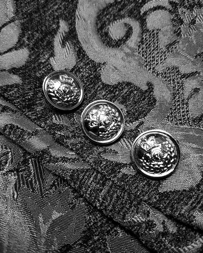 Sort og hvidt billede af tre dekorative knapper på et mønstret stof. Elegant design, vintage stil, tekstilmode, detaljeret broderi.