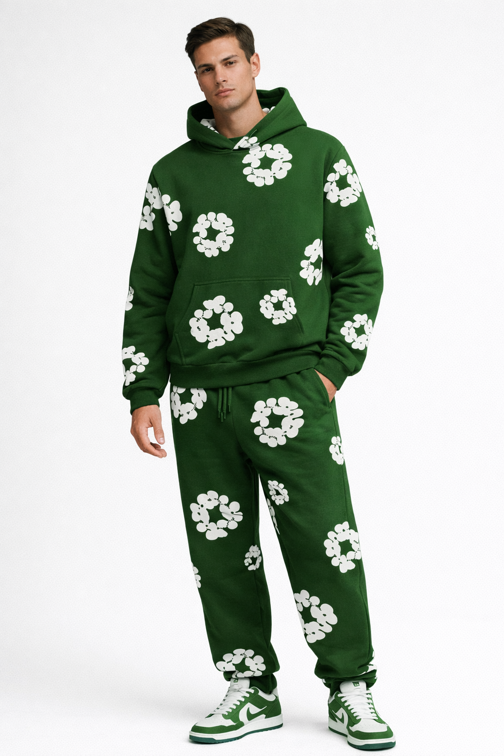 Mand iført grøn hættetrøje og bukser med hvide blomstermønstre, matchende grønne sneakers. Moderne streetwear, afslappet stil, trendy tøj.