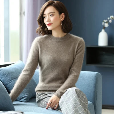 Kvinde i brun uldtrøje sidder på blå sofa, moderne stueindretning, plaid bukser, kort brunt hår, minimalistisk stil, elegant og afslappet look.