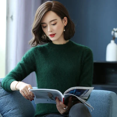 Kvinde i grøn sweater læser magasin på blå sofa i moderne stue. Elegant indretning, naturligt lys, afslappet atmosfære.