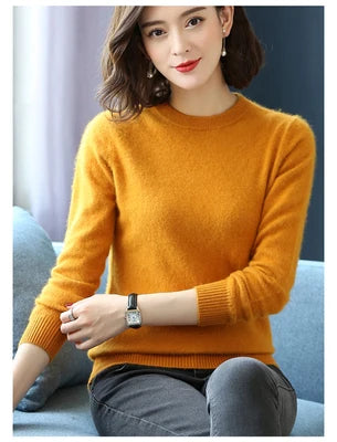 Kvinde i sennepsgul sweater, sidder på blå sofa. Hun har kort, brunt hår og bærer et armbåndsur. Perfekt til efterårs- og vintermode.