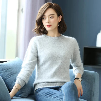 Kvinde i grå sweater sidder på sofa, moderne indretning, kort brunt hår, afslappet stil, naturligt lys, stilfuldt og elegant look.