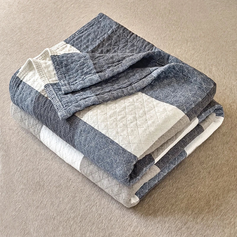 Grå og hvid quiltet plaid på beige baggrund, blødt og stilfuldt design, perfekt til stueindretning og hygge.