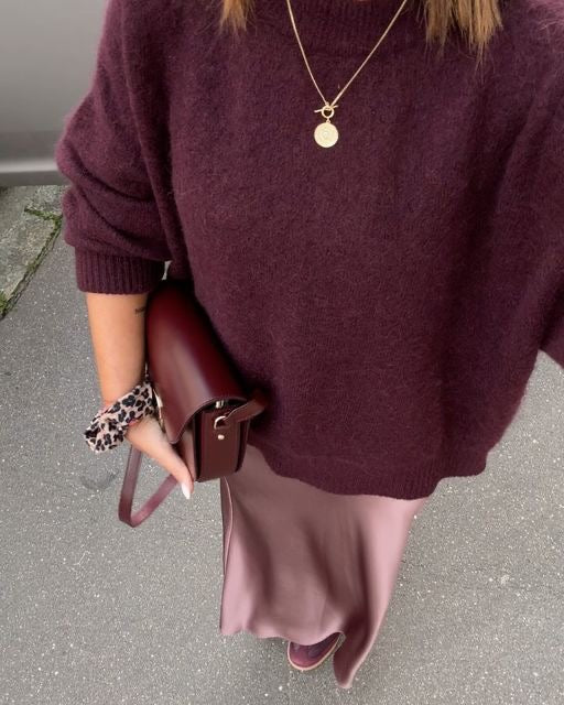 Kvinde iført bordeaux sweater og nederdel, bærer matchende taske. Mode, efterårstøj, stilfuldt look, trendy accessories, elegant outfit.