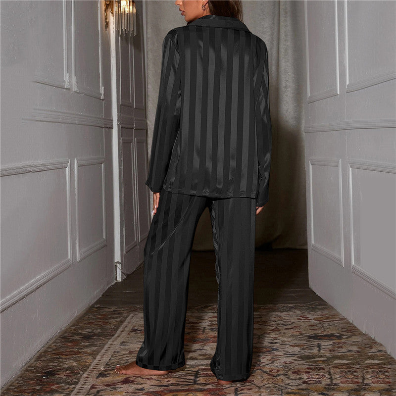 Kvinde iført sort, stribet pyjamas i silke står i en elegant gang. Luksuriøst nattøj, komfortabelt design, moderne stil.