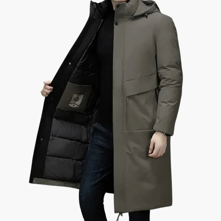 Person iført lang, olivengrøn vinterjakke med hætte og sorte detaljer. Jakken er åben, viser sort foring. Perfekt til koldt vejr.