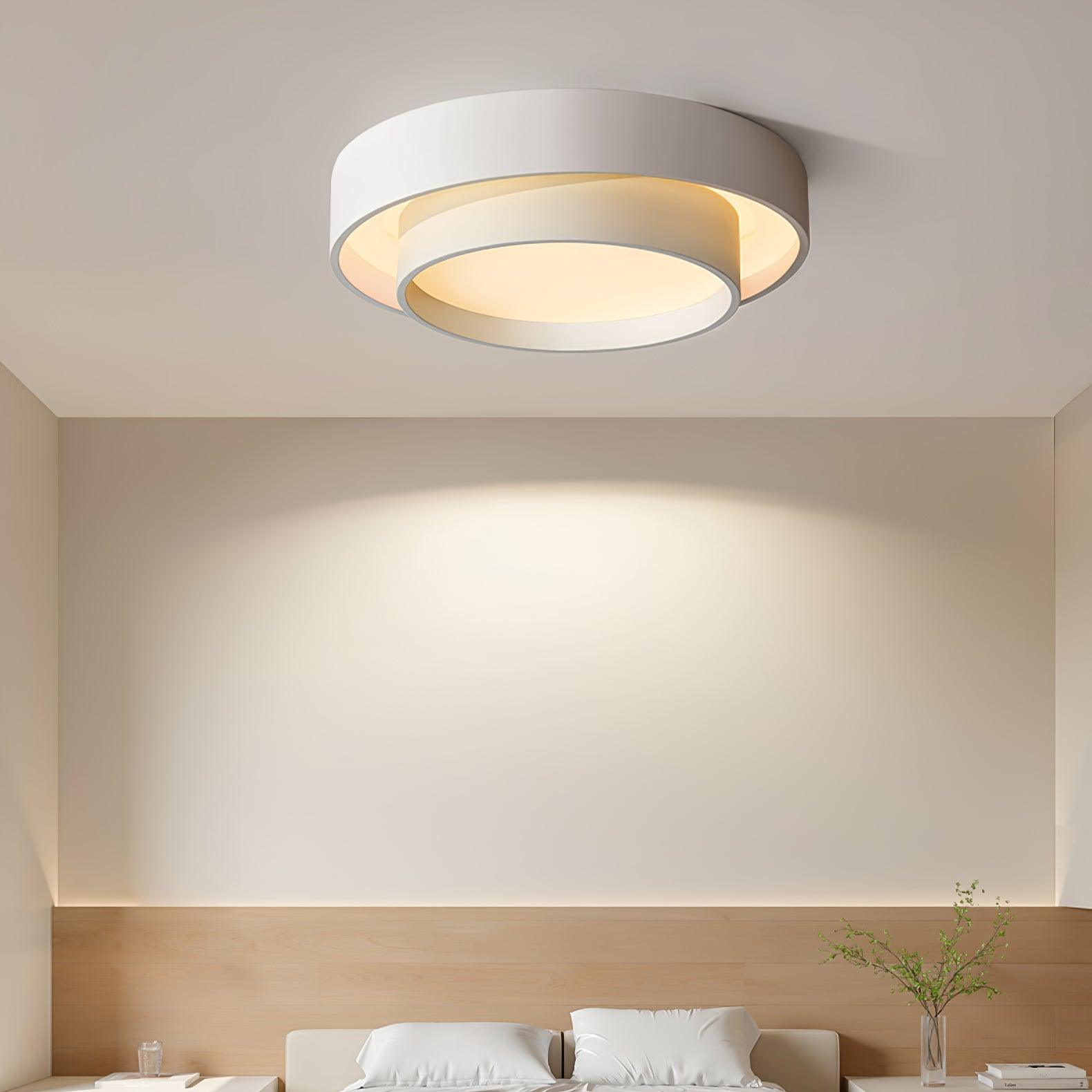 Moderne rund loftlampe i hvid med indbygget LED-lys, monteret i et minimalistisk soveværelse. Energibesparende belysning, stilfuldt design.