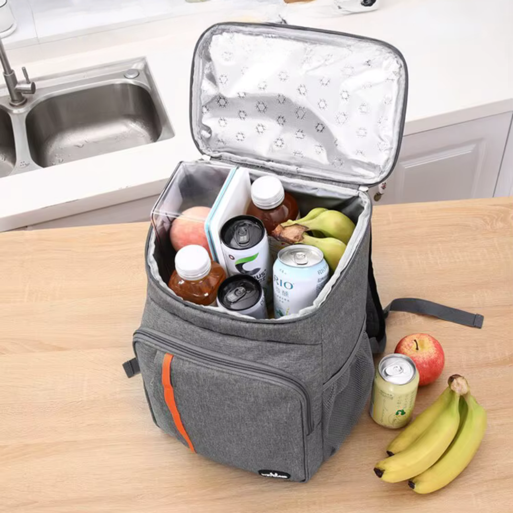 Grå køletaske på køkkenbord fyldt med drikkevarer, bananer og æbler. Perfekt til picnic, udflugter og opbevaring af mad og drikkevarer.