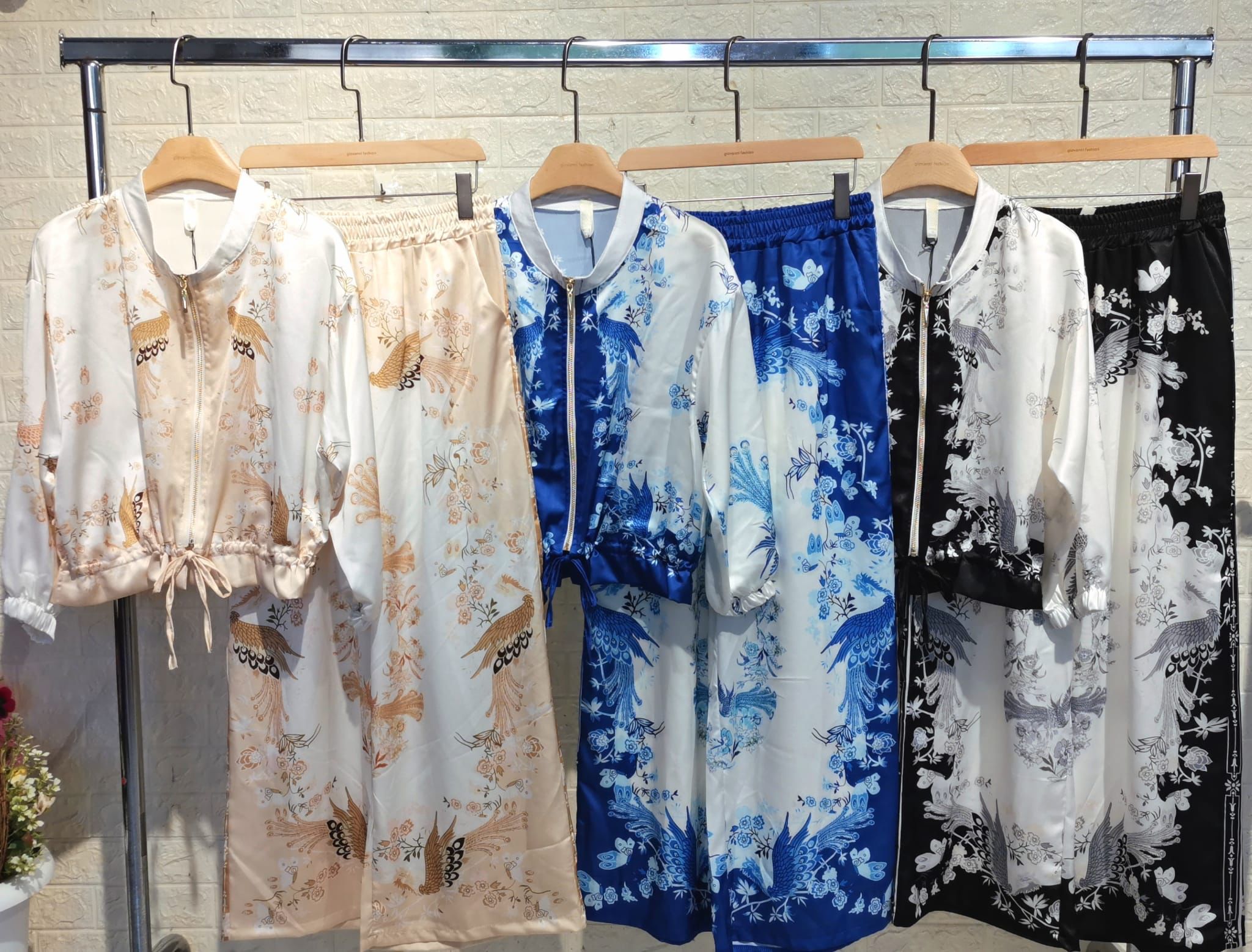 Fem kimonoer i forskellige farver og mønstre hænger på en tøjstang. Silkeagtigt stof med blomster- og sommerfuglemotiver. Japansk mode, elegant design.