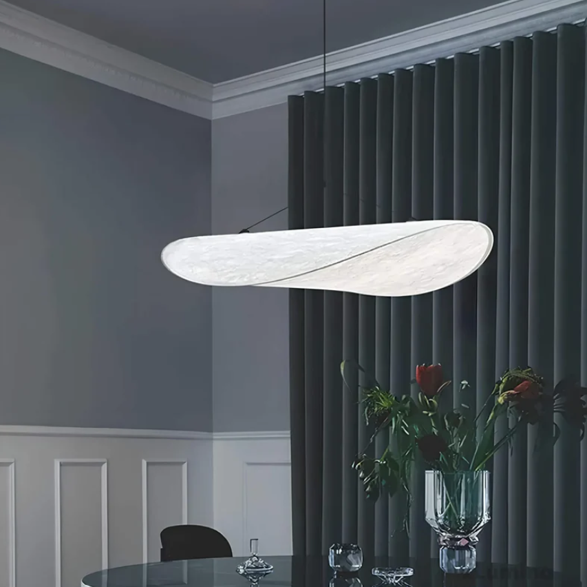 Moderne hvid loftlampe i minimalistisk design hænger over et elegant spisebord med blomsterdekoration, grå vægge og mørke gardiner.