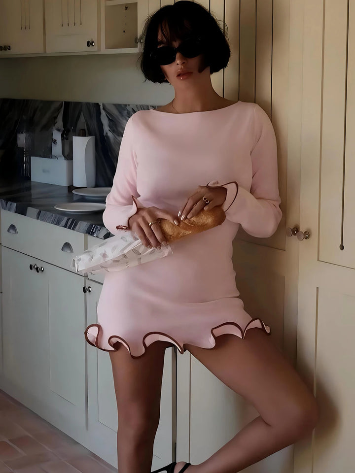 Kvinde i lyserød kjole med bølget kant, holder en croissant i køkken. Moderne køkkenindretning, solbriller, kort sort hår. Fashionabelt look.