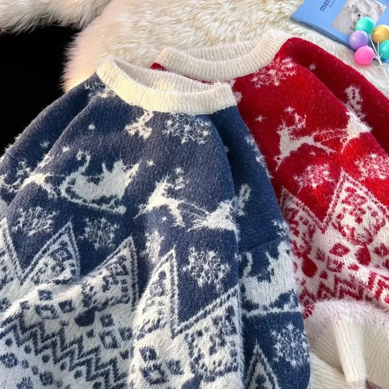 To julesweatre i blå og rød med rensdyr- og snefnugmønster, liggende på en hvid pelsbaggrund. Perfekt til vintermode og julehygge.