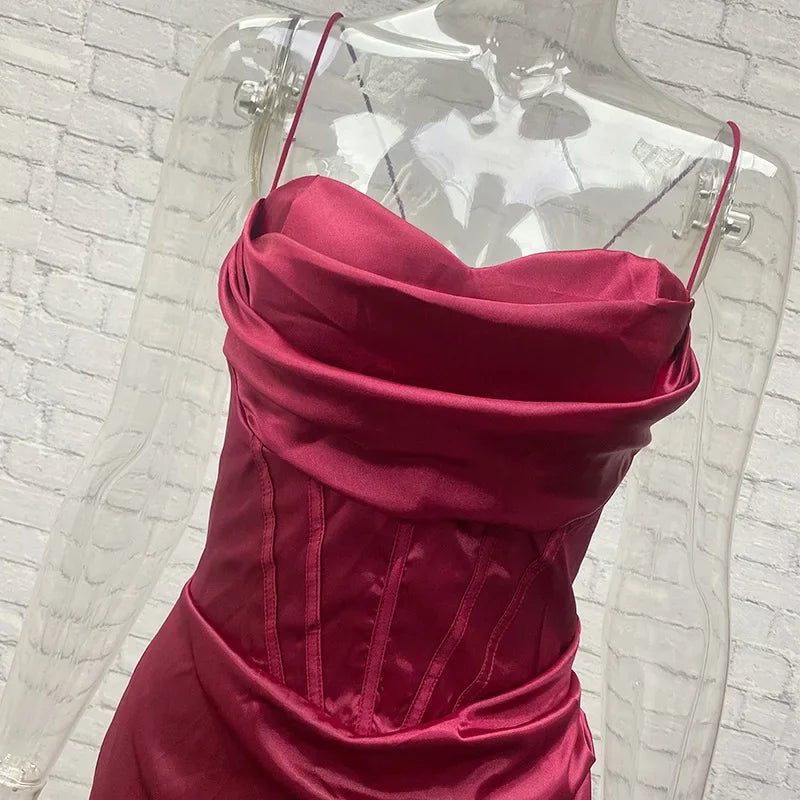 Rød satin corsagekjole på gennemsigtig mannequin mod hvid murstensvæg. Elegant design, spaghetti-stropper, perfekt til festlige lejligheder.