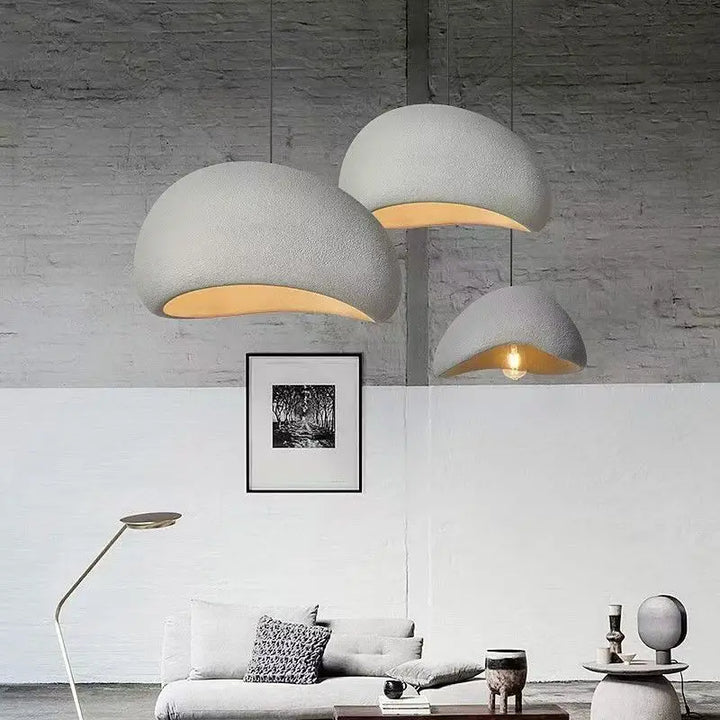 Moderne stue med tre store, hvide hængelamper, minimalistisk sofa, gulvlampe og kunst på væggen. Skandinavisk design, stilfuld indretning.