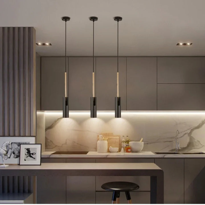 Moderne køkken med grå skabe, marmor backsplash og tre sorte pendellamper. Minimalistisk indretning med skammel og kunstværk på bordet.