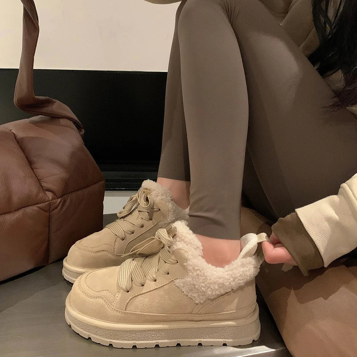 Beige sneakers med pelsfor, kvinde iført leggings, sidder ved brun taske. Komfortable vinterstøvler, moderigtigt fodtøj til koldt vejr.
