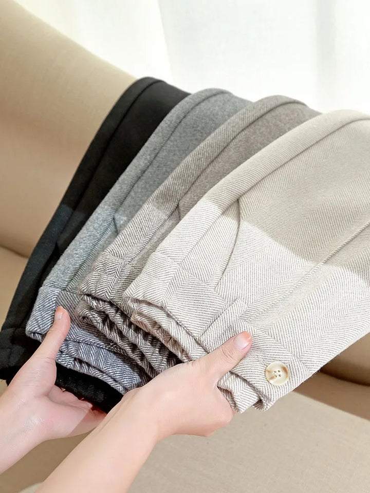 Hænder holder en stak af uldbukser i forskellige nuancer af grå og beige på en beige sofa. Høj kvalitet, stilfulde herrebukser, vintermode.