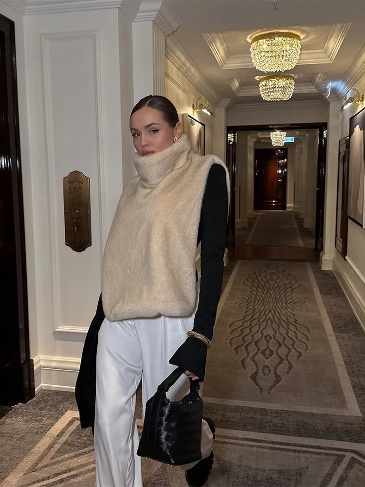 Kvinde i beige vest og hvide bukser i elegant hotelgang med lysekroner. Mode, stilfuldt tøj, moderne kvindemode, luksuriøst interiør.