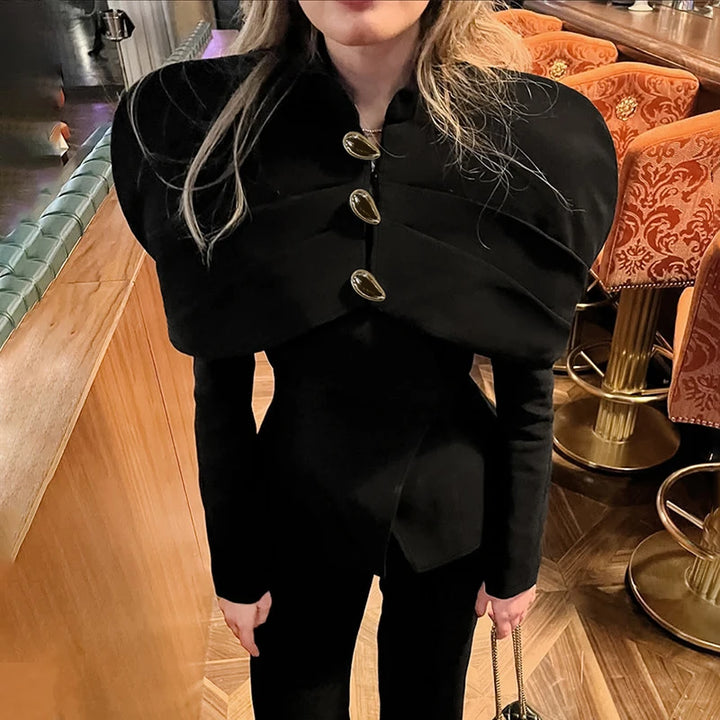 Kvinde i elegant sort jakke med store knapper, står i en stilfuld bar med orange stole. Mode, stilfuldt tøj, moderne design, aftenudgang.