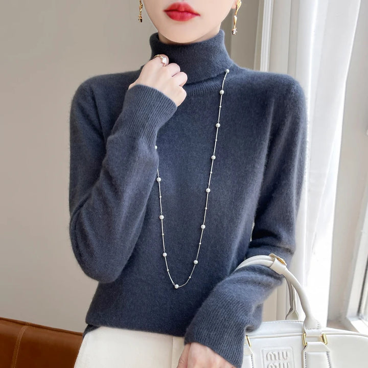 Kvinde i grå rullekrave sweater med perlekæde, holder hvid taske. Elegant mode, vintertøj, stilfuldt tilbehør.