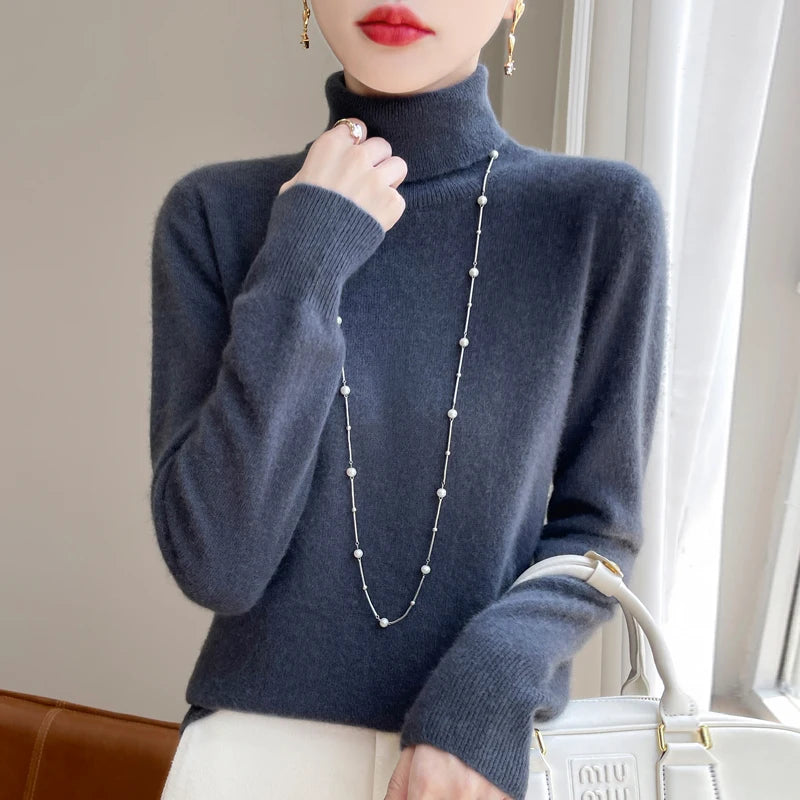 Kvinde i grå rullekrave sweater med perlekæde, holder hvid taske. Elegant mode, vintertøj, stilfuldt tilbehør.