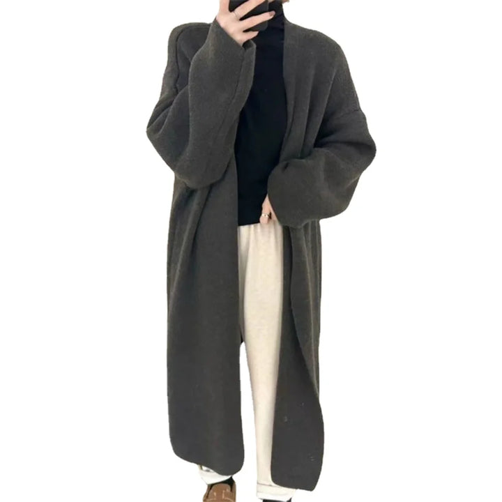 Lang, grå uldfrakke til kvinder, bæres over sort trøje og hvide bukser. Moderne vintermode, stilfuldt og varmt overtøj til kolde dage.