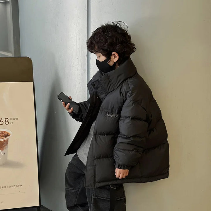 Dreng i sort dunjakke og maske kigger på smartphone. Vintermode, børnetøj, udendørs, moderne stil.