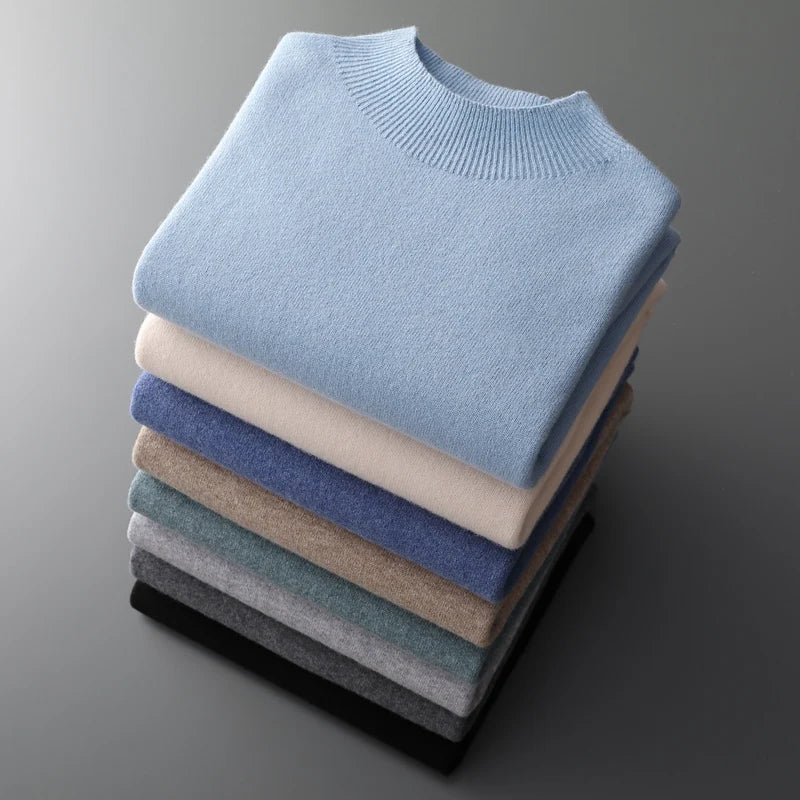Stable af farverige uldtrøjer i forskellige nuancer, herunder blå, beige og grå, stablet på en grå baggrund. Perfekt til vintermode og komfort.