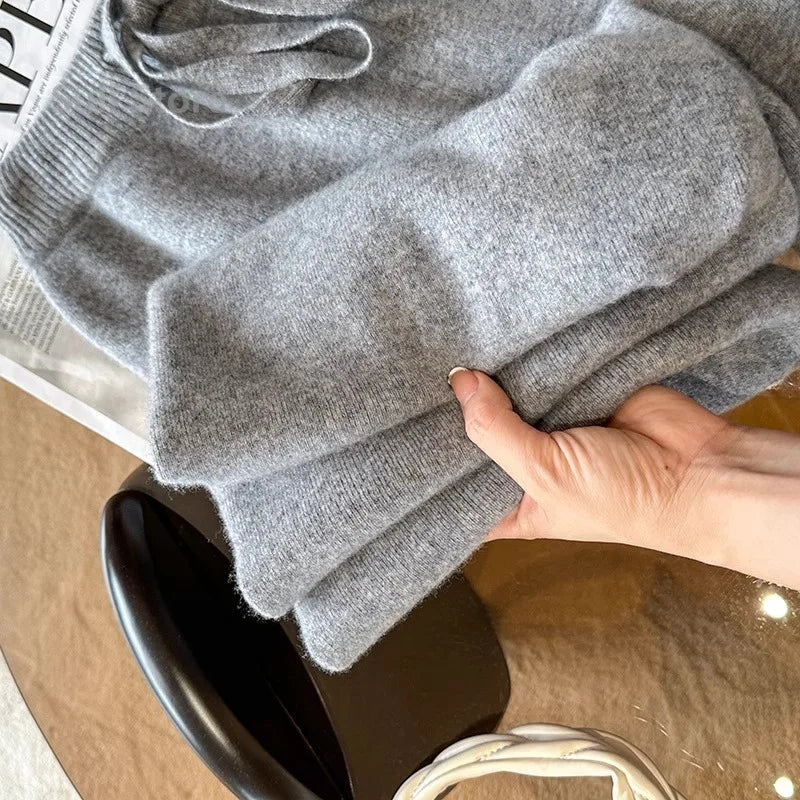 Grå uldtrøje i blødt materiale, foldet og holdt af en hånd på et bord. Perfekt til vintermode og komfortabelt tøj.