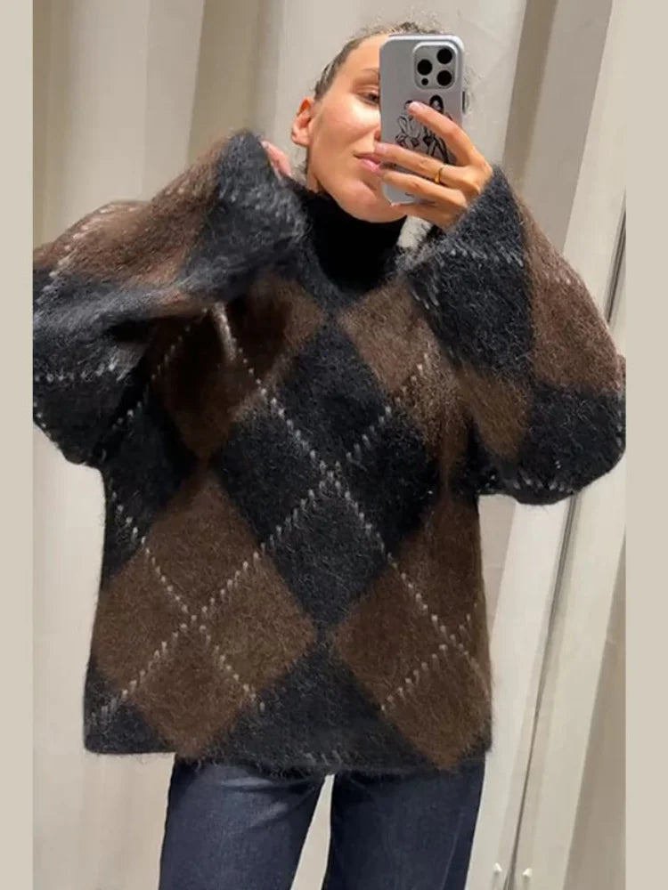 Kvinde iført ternet, oversize sweater i brune og sorte nuancer, tager selfie med smartphone. Moderne vintermode, casual stil, striktrøje.