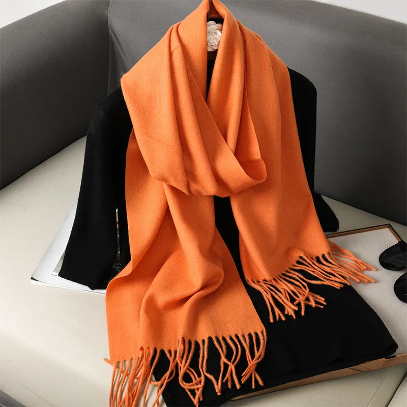 Orange cashmere tørklæde med frynser på en sort sofa. Blødt og luksuriøst tilbehør, perfekt til efterår og vinter. Ideel til modebevidste.