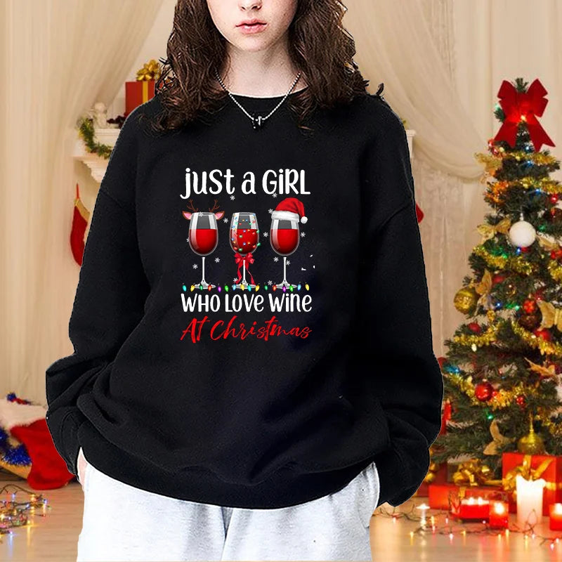 Kvinde i sort sweatshirt med teksten "Just a girl who loves wine at Christmas", foran juletræ og dekorationer. Perfekt til julegaveidéer.