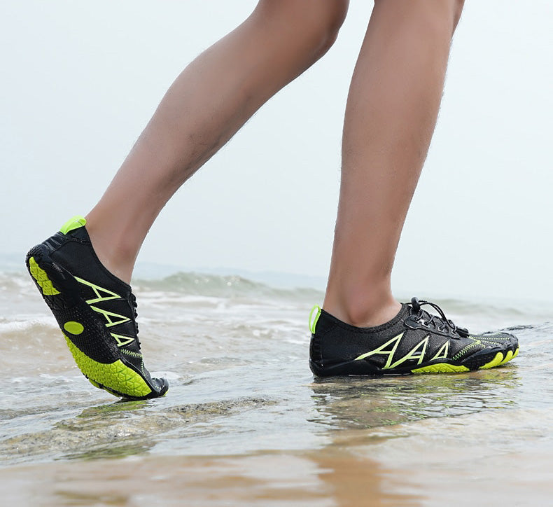 Person iført sorte og grønne vandsko går på strand. Komfortable, lette sko til strandaktiviteter. Ideelle til vandsport og sommerbrug.