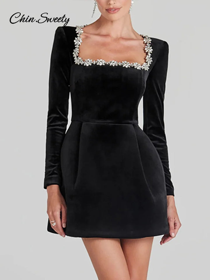 Kvinde i sort fløjlskjole med firkantet halsudskæring og blomsterdetaljer. Elegant aftenkjole, lange ærmer, stilfuldt design.