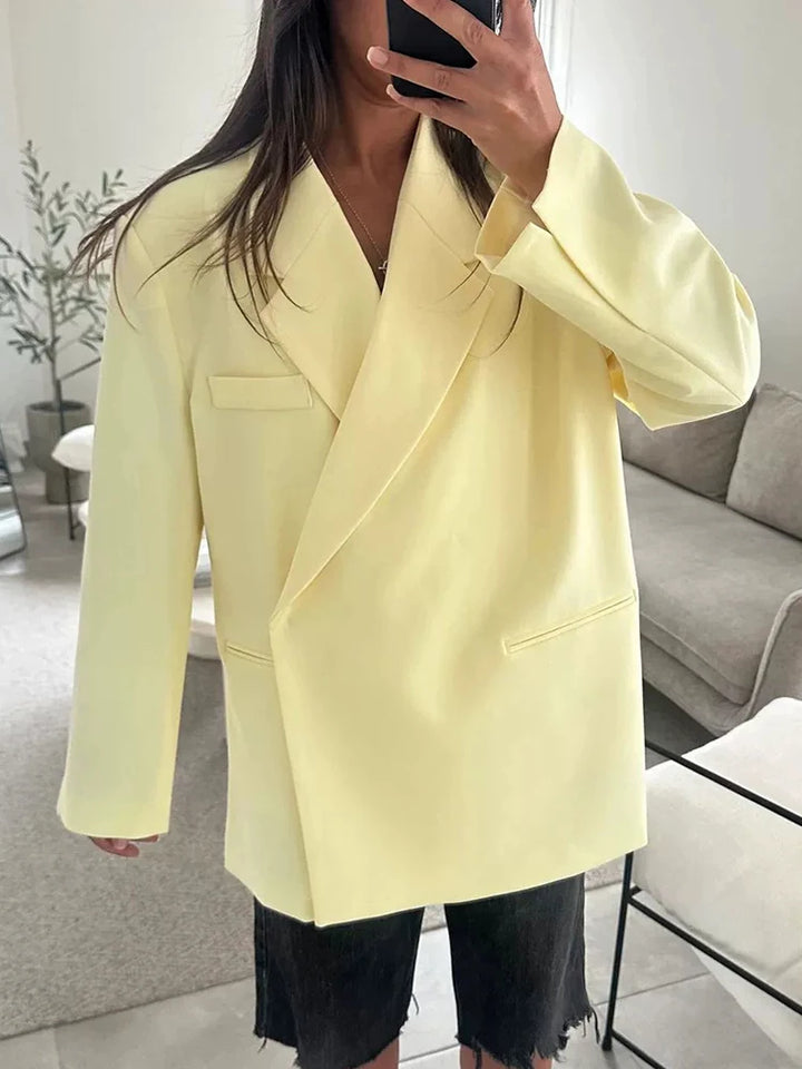 Kvinde iført lysegul oversized blazer, sort denim shorts, moderne stueindretning i baggrunden. Trendy mode, minimalistisk stil, casual elegance.