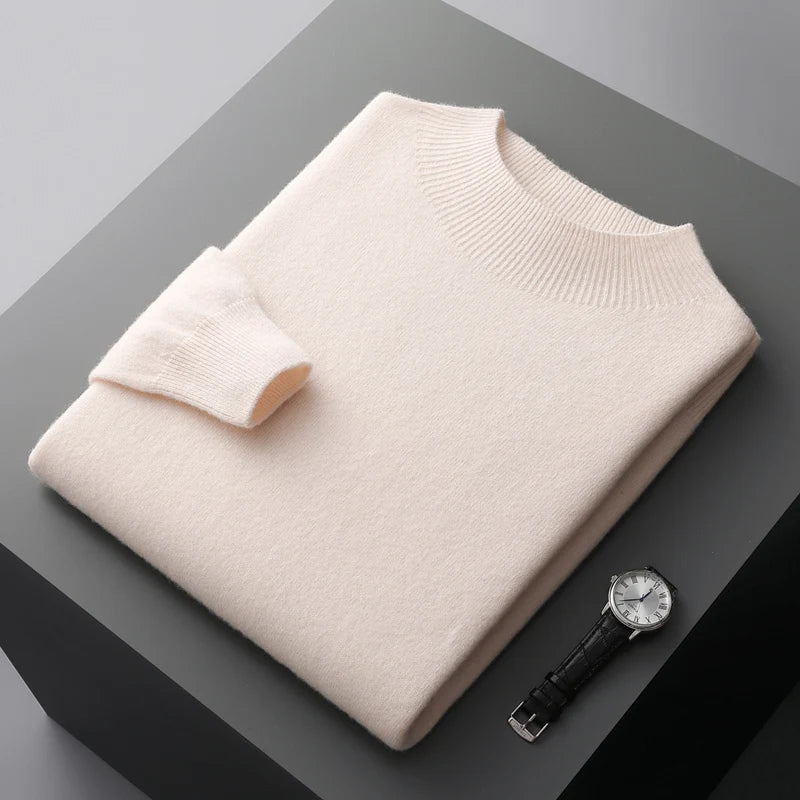 Beige cashmere sweater foldet på grå overflade ved siden af sort læderur. Luksuriøs striktrøje, blødt materiale, elegant design.
