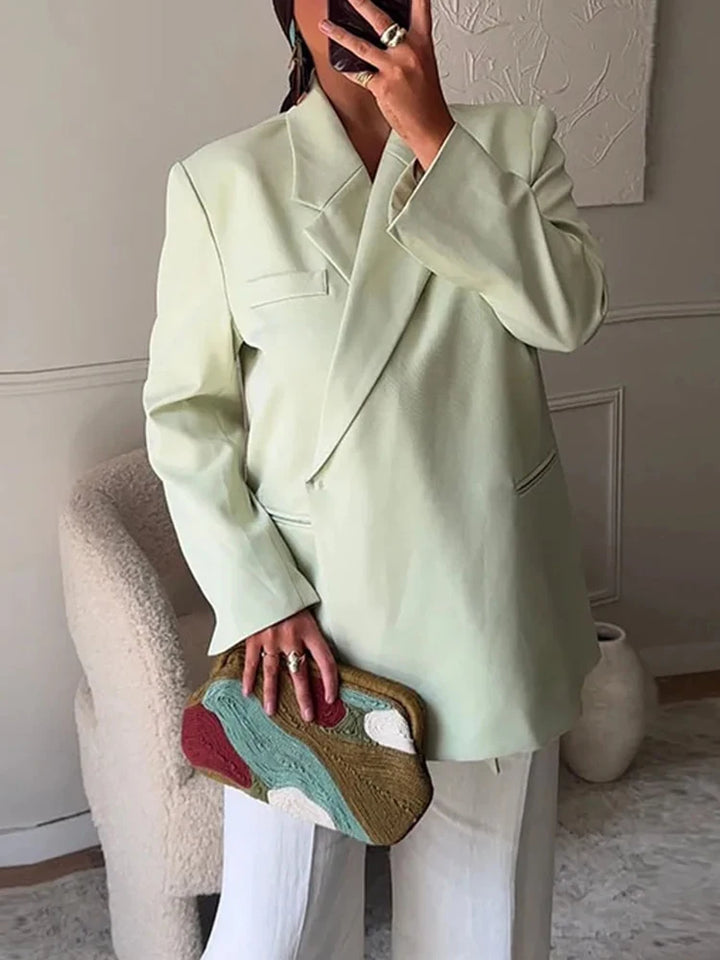 Dame i lysegrøn blazer og hvide bukser holder en farverig clutch. Moderne mode, stilfuldt outfit, elegant tøjvalg, trendy accessories.