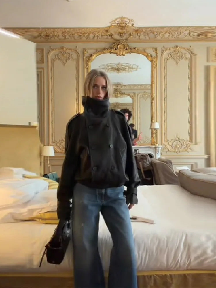 Kvinde i sort jakke og blå jeans står i elegant hotelværelse med gyldne detaljer og stor spejl. Luksuriøs indretning, rejse, mode.