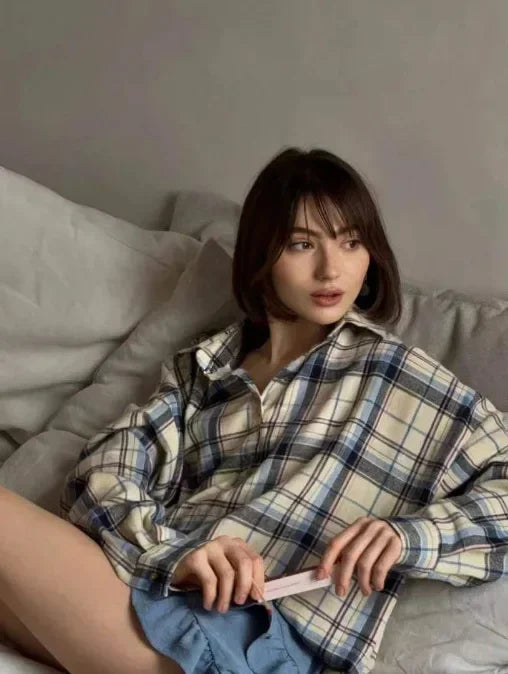 Ung kvinde i ternet skjorte sidder på sofa, ser til siden. Kort, mørkt hår. Afslappet hjemmestil. Indendørs portræt.