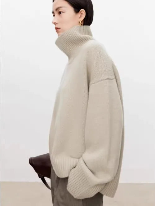Kvinde iført beige, oversized rullekravesweater, poserer mod hvid baggrund. Moderne mode, minimalistisk stil, vintertøj, komfortabelt design.