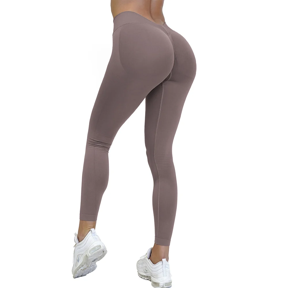 Dame iført brune leggings og hvide sneakers, set bagfra. Komfortabelt træningstøj til fitness og yoga. Sportstøj til kvinder.