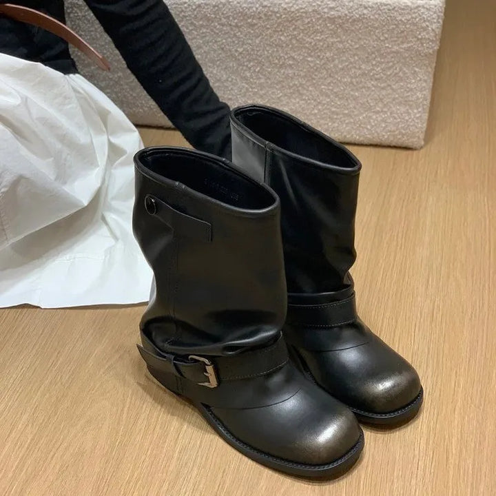 Sort læderstøvler med spænde på trægulv, moderne design, stilfuldt fodtøj til efterår og vinter, perfekt til modebevidste kvinder.