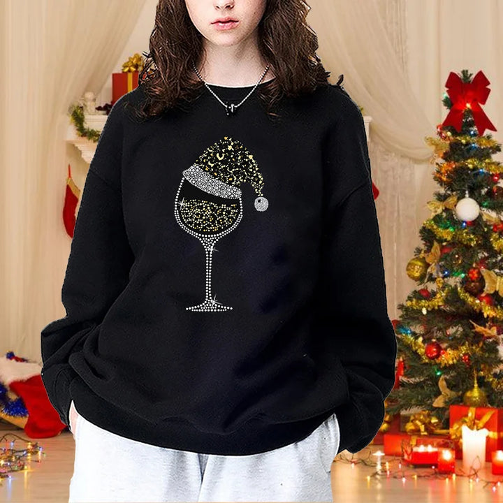 Kvinde i sort sweatshirt med glitrende vinglas og nissehue design, foran juletræ. Perfekt til julefest, vintermode, trendy tøj.