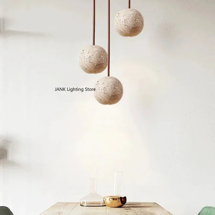 Tre moderne, runde loftslamper i beige hænger over et minimalistisk træbord med glasdekorationer. Skandinavisk design, stilfuld belysning.