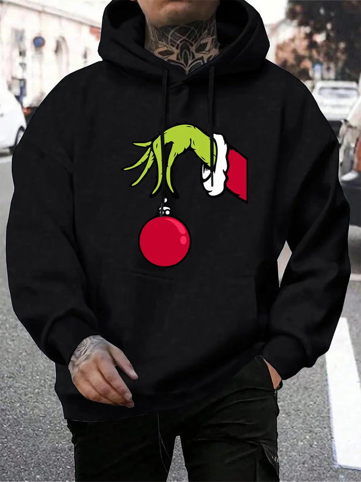 Sort hættetrøje med Grinch-motiv, der holder en rød julekugle. Perfekt til jul, streetwear og vintermode. Unikt design til fans af juleklassikere.