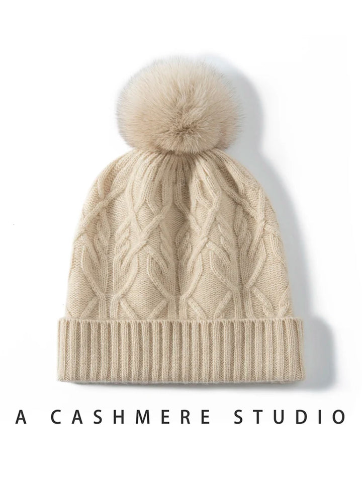 Beige kashmirhue med kabelstrik og pompon, elegant vintertilbehør, varm og stilfuld, perfekt til kolde dage.