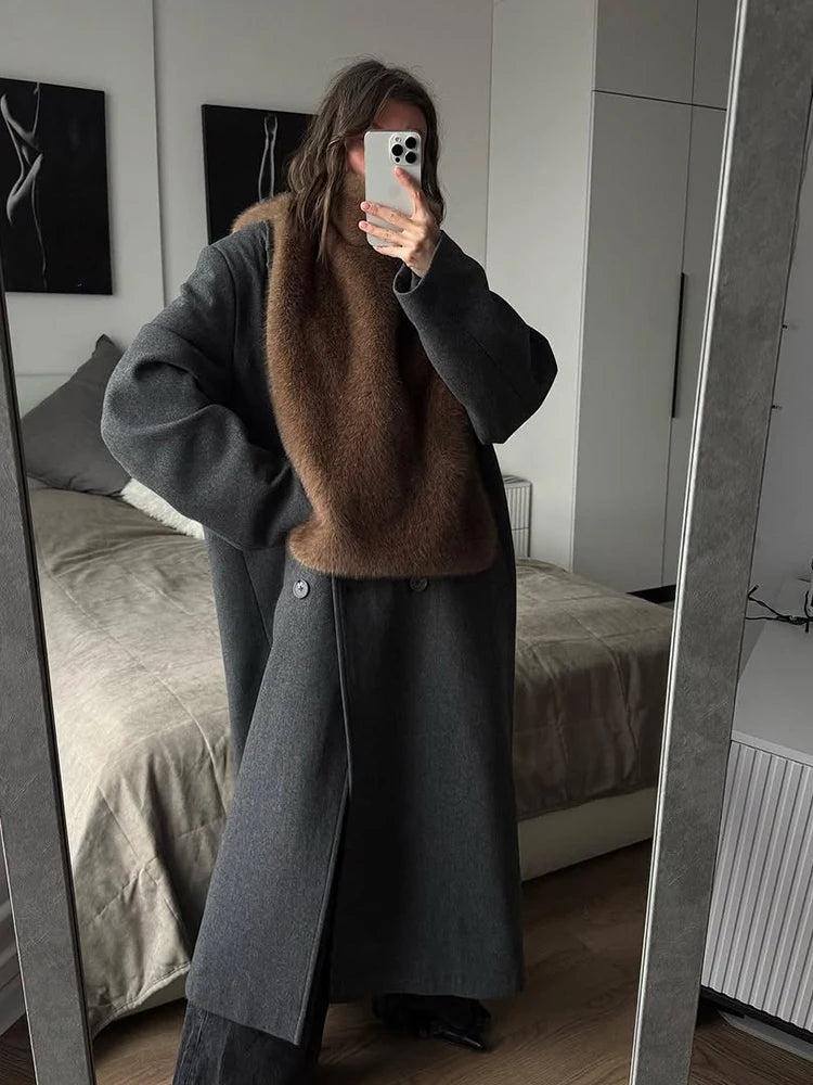 Kvinde iført grå frakke med brun pelskrave tager spejlbillede i moderne soveværelse. Stilfuldt vinteroutfit, mode, indretning.