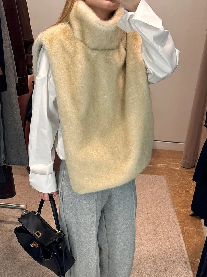 Kvinde iført hvid skjorte og beige pelsvest, grå bukser, holder sort håndtaske. Mode, vintertøj, stilfuldt outfit, shopping.