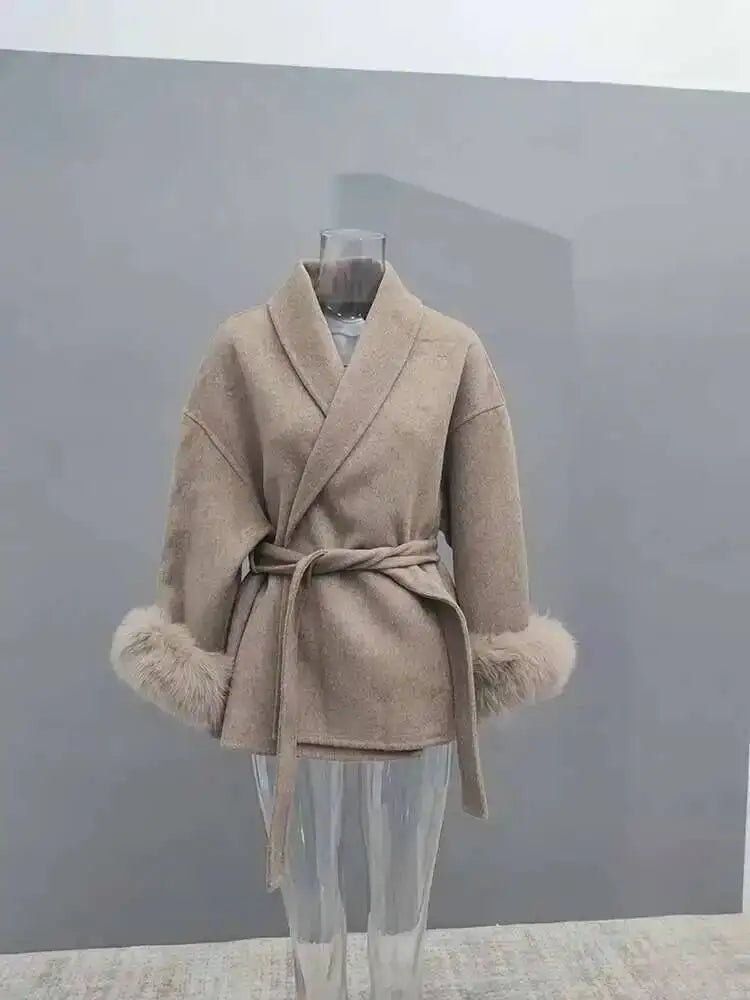 Beige uldfrakke med bælte og pelsmanchetter på gennemsigtig mannequin. Elegant vinterjakke, moderne design, stilfuld overtøj til kvinder.
