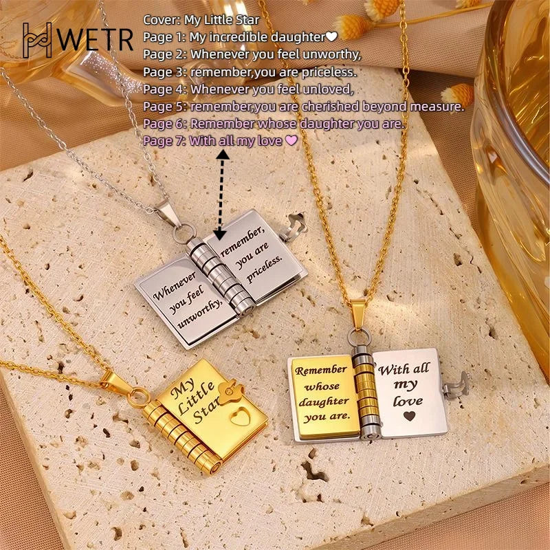 To halskæder med vedhæng, der ligner bøger, på en træoverflade. Indgraveret tekst: "My Little Star" og "Remember whose daughter you are."